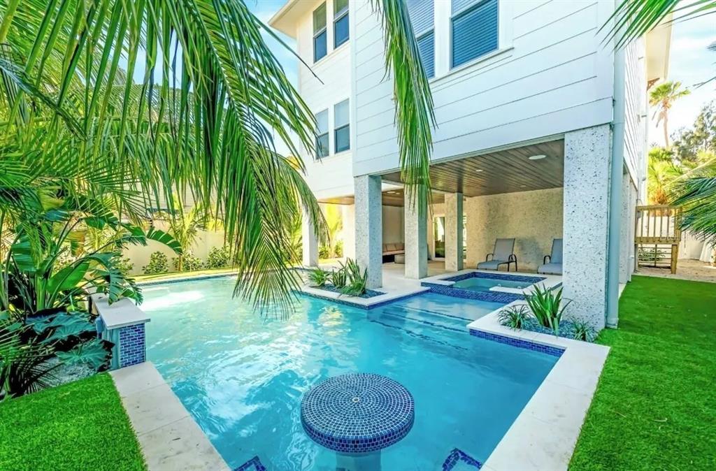 A swimming pool and hot tub sit beneath a white house with palm trees — 2403 AVENUE C, BRADENTON BEACH, FL