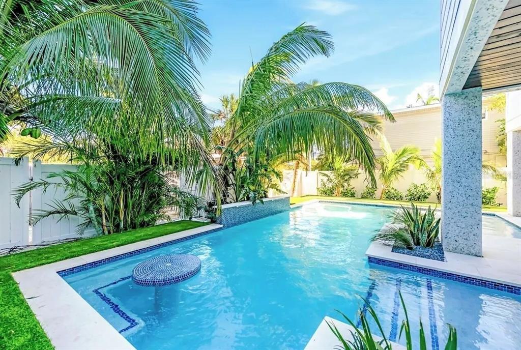 A swimming pool with a built-in table sits in a backyard surrounded by palm trees — 2403 AVENUE C, BRADENTON BEACH, FL