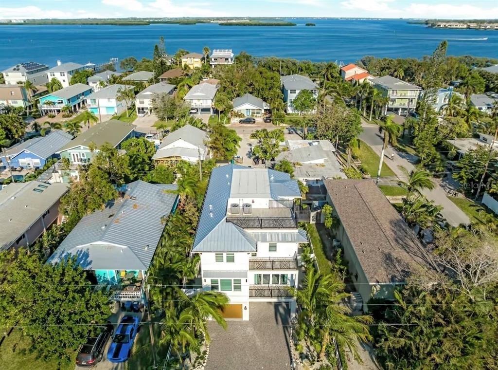 An aerial view shows a multi-story white house with a metal roof near water — 2403 AVENUE C, BRADENTON BEACH, FL