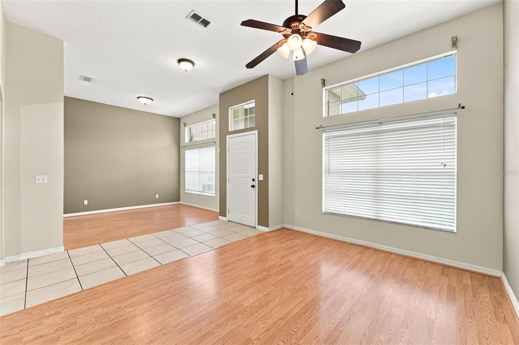 A living room with light wood flooring, tile entryway, ceiling fan, and large windows — 614 RED MULBERRY DRIVE, DELTONA, FL