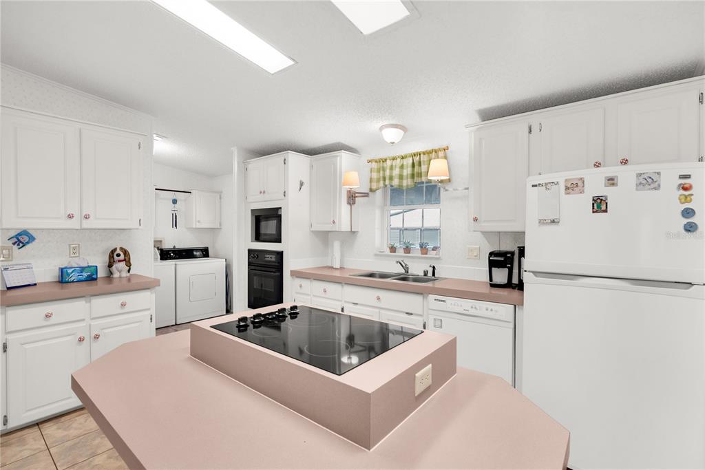 A kitchen features white cabinetry, pink countertops, a central island cooktop, and white appliances — 222 SUE AVENUE, DAVENPORT, FL