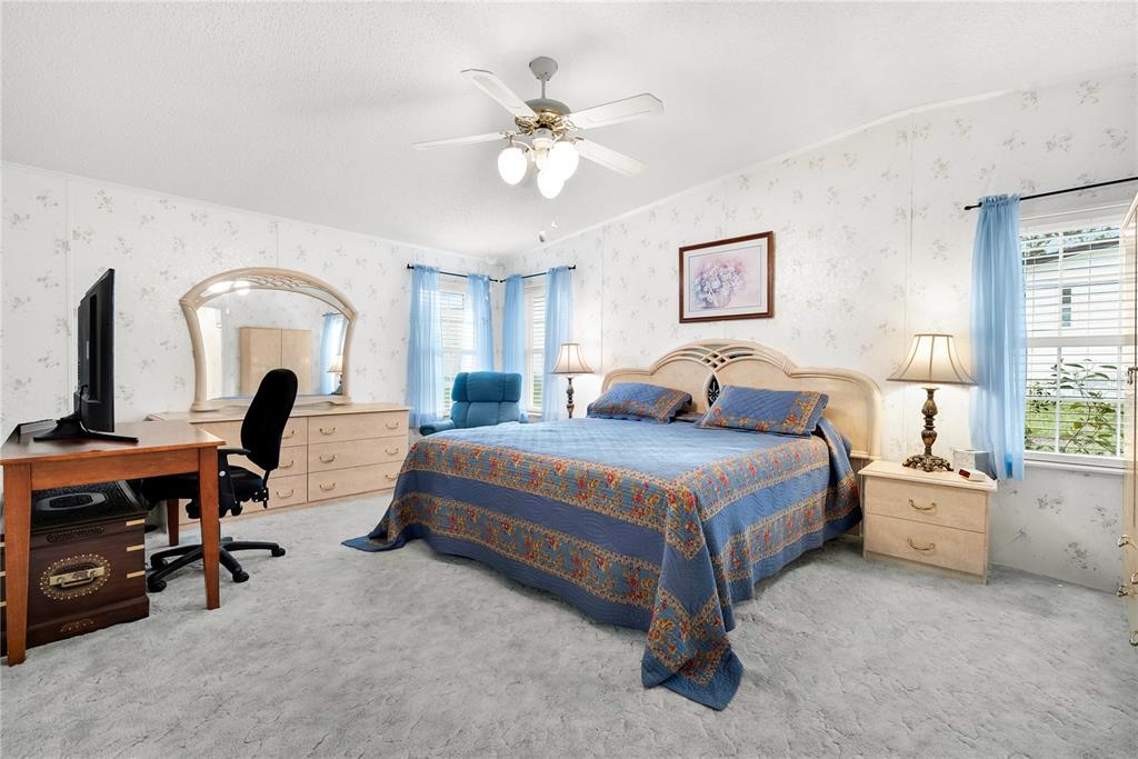 A bedroom features a blue bedspread, floral wallpaper, a ceiling fan, and a wooden desk — 222 SUE AVENUE, DAVENPORT, FL