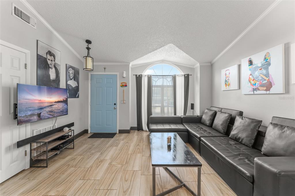 A living room features light wood-look tile floors, a black sectional sofa, and a blue door — 961 MILLENBECK AVENUE, DELTONA, FL