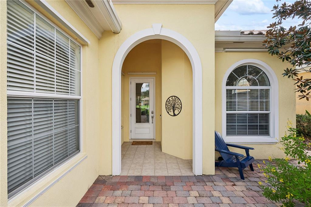 A yellow stucco home entrance features a brick paver patio, arched doorway, and blue chair — 11962 GENNARO LN, ORLANDO, FL