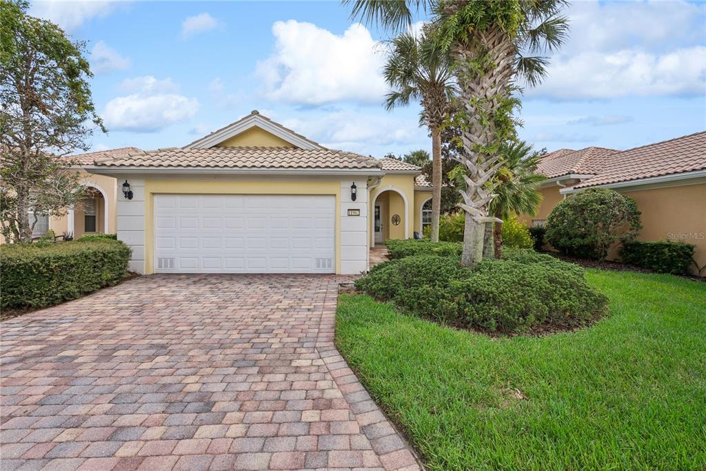 A yellow single-story house with a two-car garage, paver driveway, and a palm tree — 11962 GENNARO LN, ORLANDO, FL