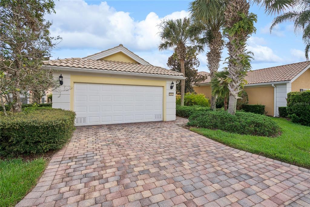 A single-story house exterior features a two-car garage, a paver driveway, and palm trees — 11962 GENNARO LN, ORLANDO, FL