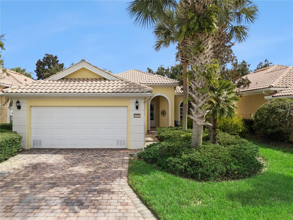 A yellow house with a two-car garage, a brick driveway, and a palm tree — 11962 GENNARO LN, ORLANDO, FL