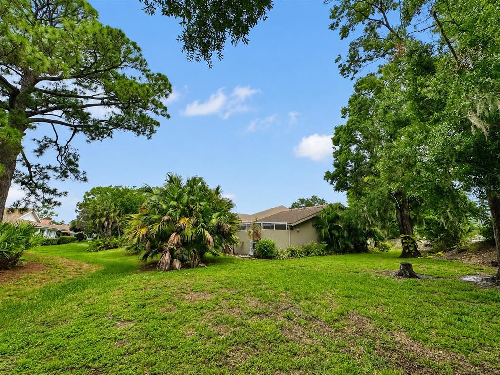 A grassy backyard features a house with a screened lanai surrounded by trees and palms — 5608 37TH STREET E UNIT 26, BRADENTON, FL