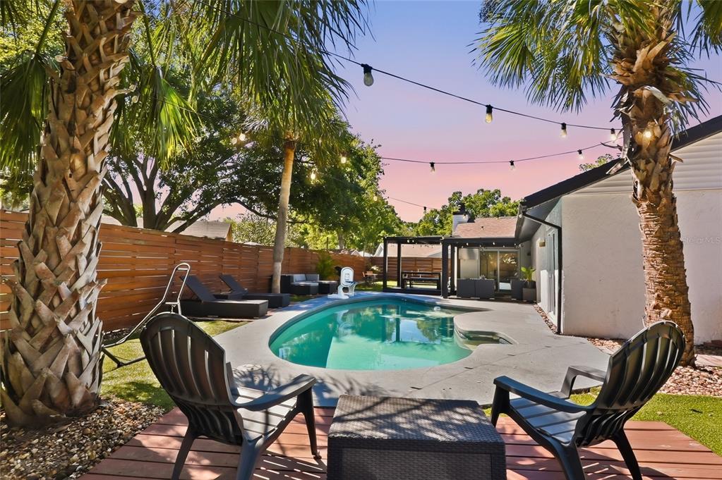 A backyard features a swimming pool, palm trees, string lights, and patio furniture on decking — 4606 BUCKEYE ROAD, TAMPA, FL