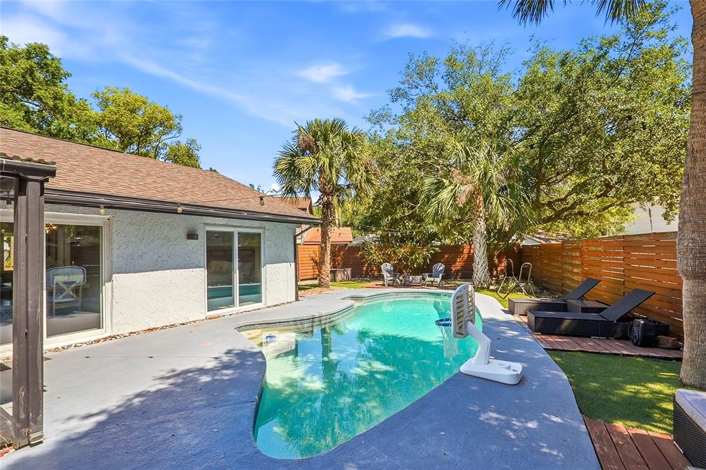 A backyard features a swimming pool, a concrete patio, lounge chairs, and a wooden fence — 4606 BUCKEYE ROAD, TAMPA, FL