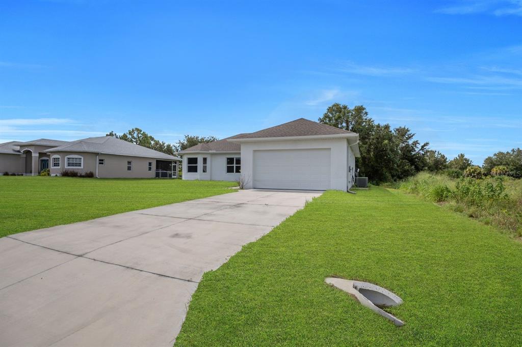 A concrete driveway leads to the garage of a single-story house with a grassy yard — 856 WILLIAM DENVER STREET, LEHIGH ACRES, FL
