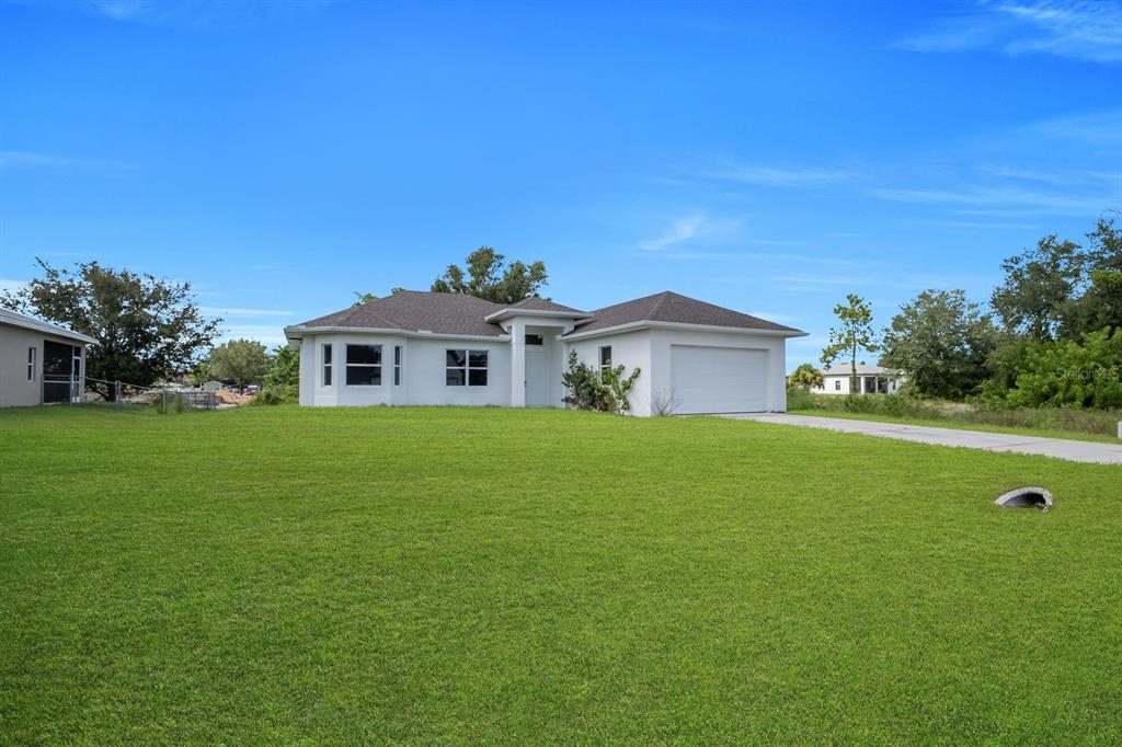 A single-story white house with a two-car garage sits on a large grassy lawn — 856 WILLIAM DENVER STREET, LEHIGH ACRES, FL