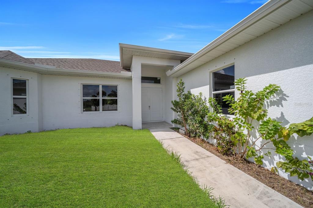 A white stucco house exterior features a front walkway leading to a double-door entryway — 856 WILLIAM DENVER STREET, LEHIGH ACRES, FL