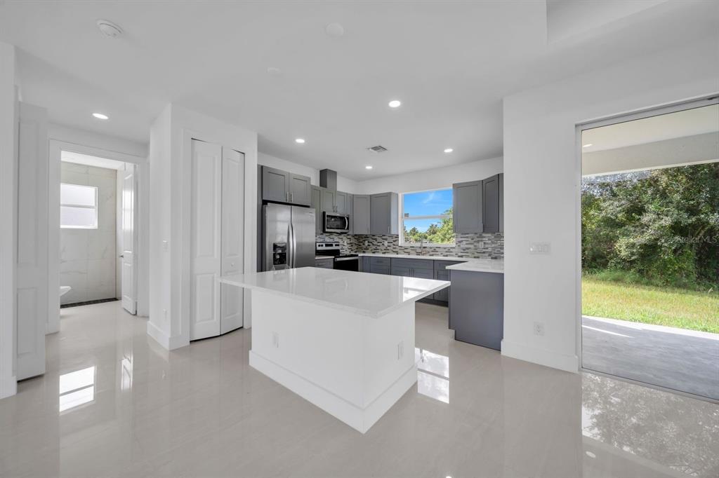 A modern kitchen features a white island, gray cabinetry, stainless steel appliances, and a sliding door — 856 WILLIAM DENVER STREET, LEHIGH ACRES, FL