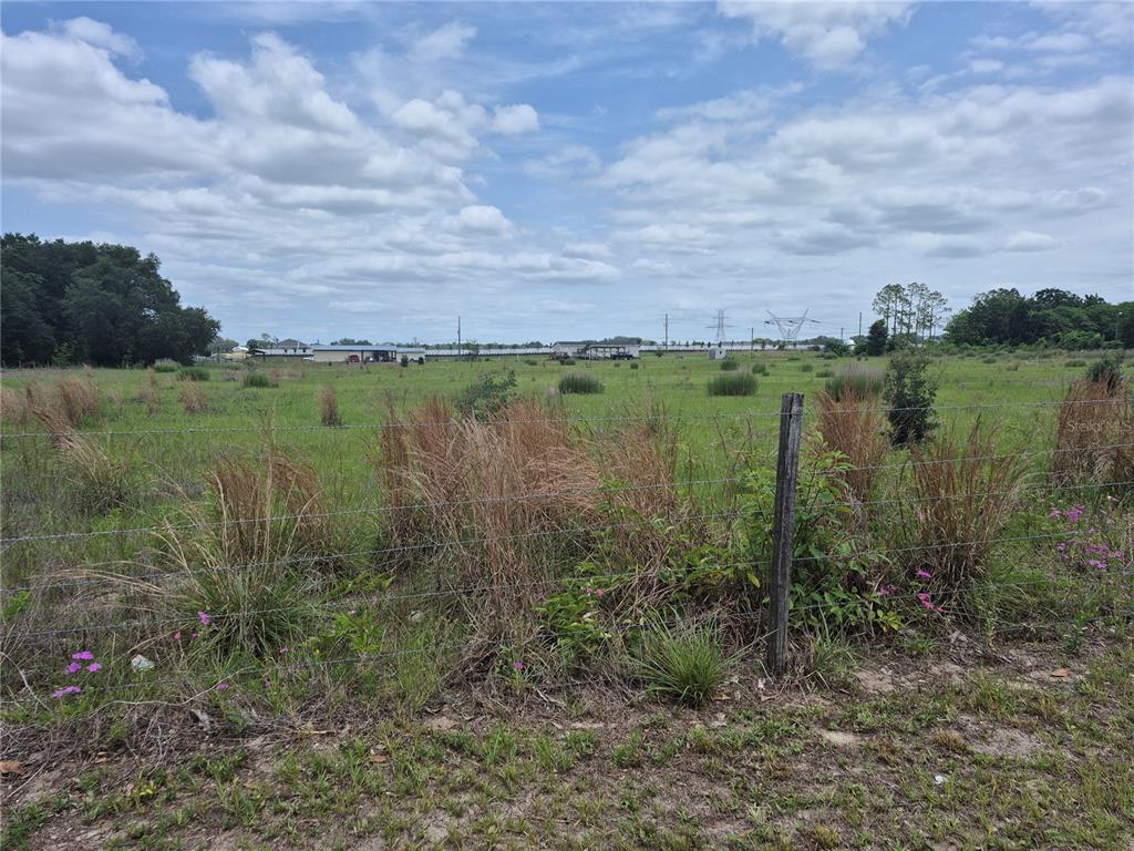A wire fence borders a grassy, open field under a cloudy blue sky — CR 229, WILDWOOD, FL