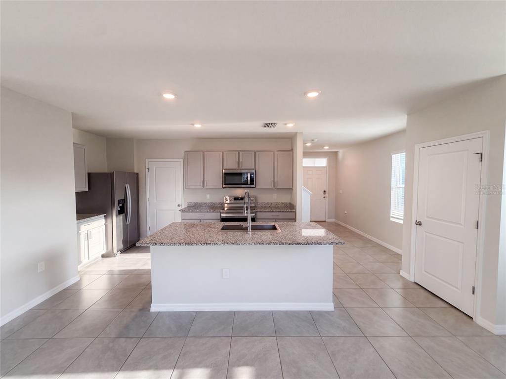 A kitchen features a granite-topped island, stainless steel appliances, light gray cabinets, and tile flooring — 16176 SOFT FERN TRACE, ODESSA, FL