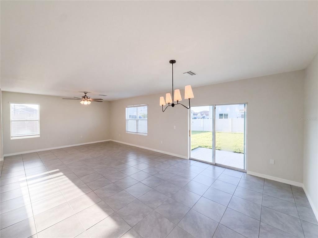 A spacious, tiled living area features a ceiling fan, a chandelier, and sliding glass doors — 16176 SOFT FERN TRACE, ODESSA, FL