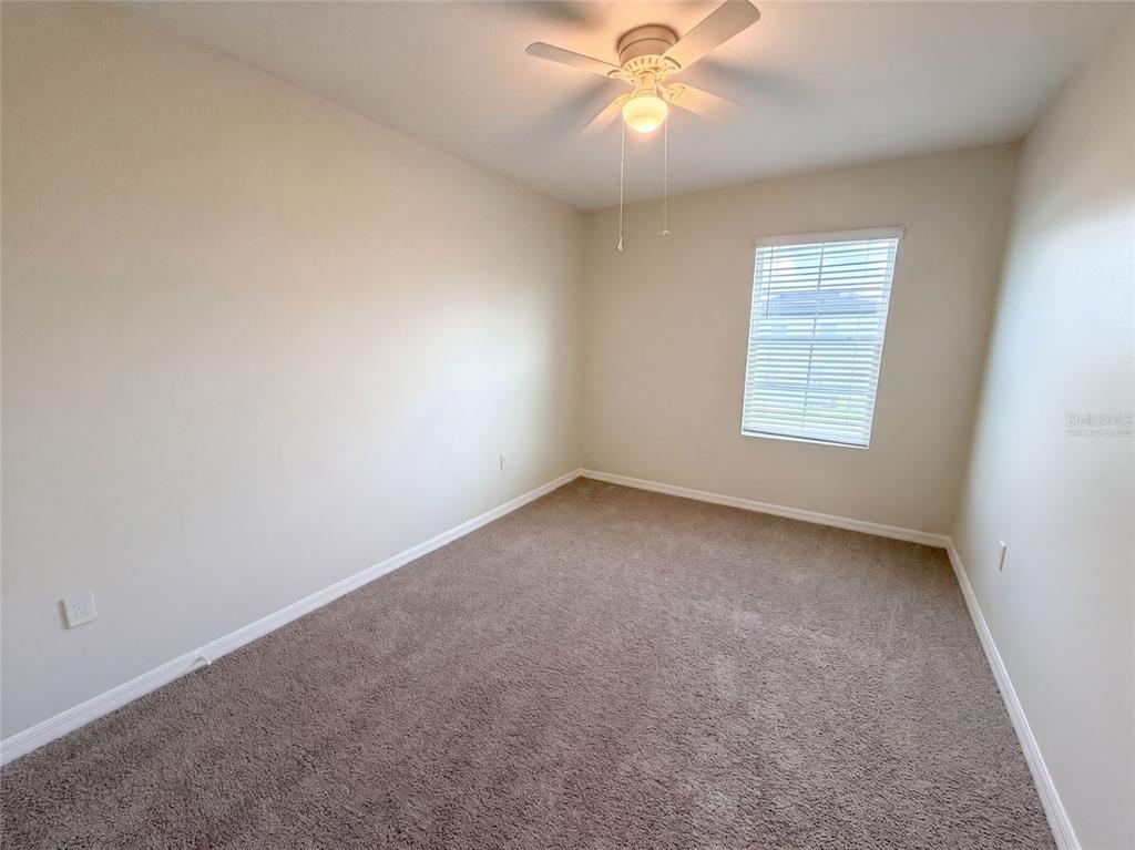 An empty bedroom features beige walls, gray carpeting, a ceiling fan, and a single window — 16176 SOFT FERN TRACE, ODESSA, FL