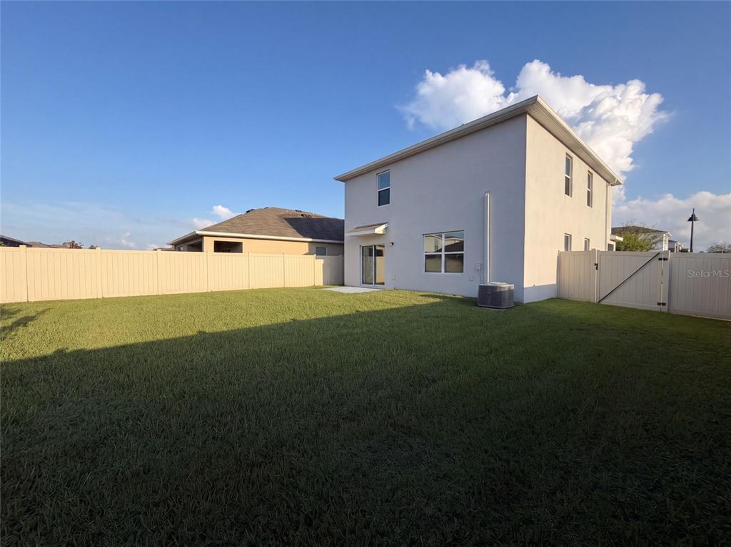 The backyard features a grassy lawn, a beige vinyl fence, and the rear of a house — 16176 SOFT FERN TRACE, ODESSA, FL