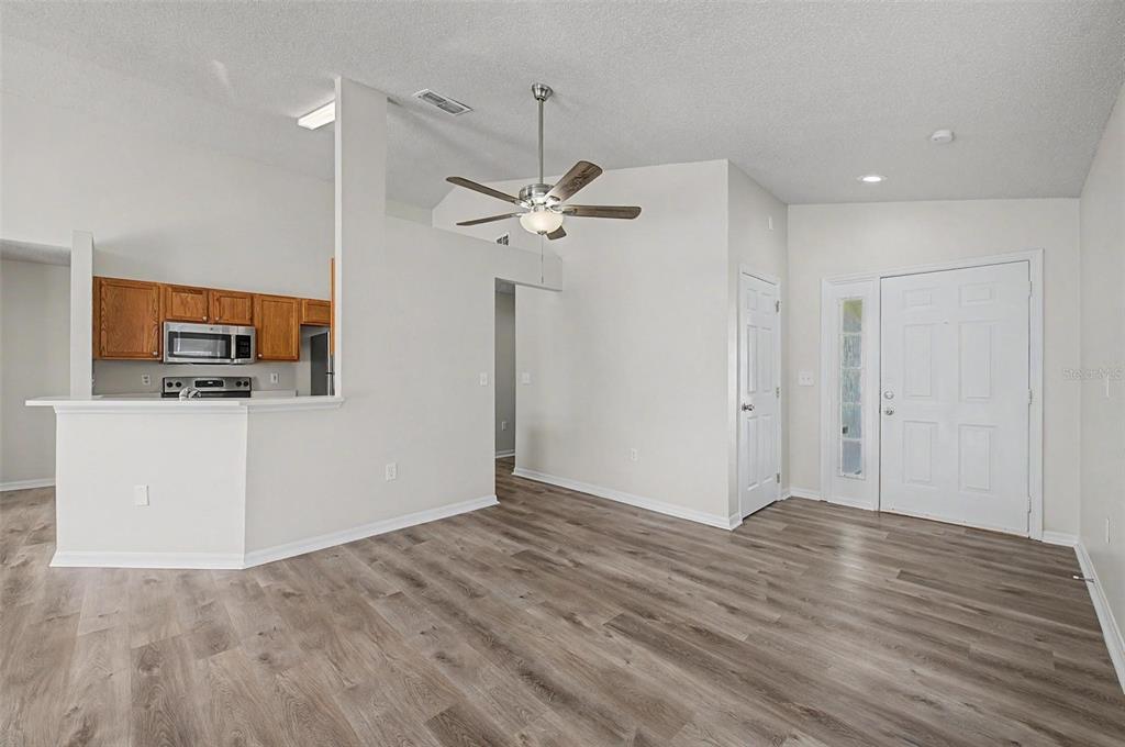 An open-concept living area features light gray wood-look flooring, a ceiling fan, and a kitchen — 421 HOLBORN LOOP, DAVENPORT, FL