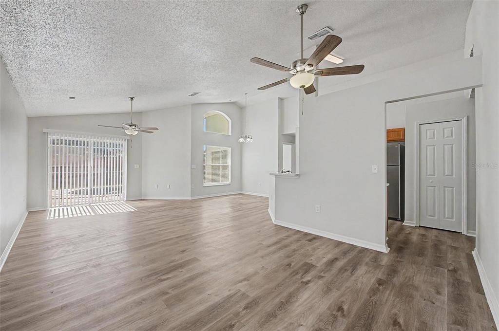 A spacious living area features light wood-look flooring, vaulted ceilings, two ceiling fans, and windows — 421 HOLBORN LOOP, DAVENPORT, FL
