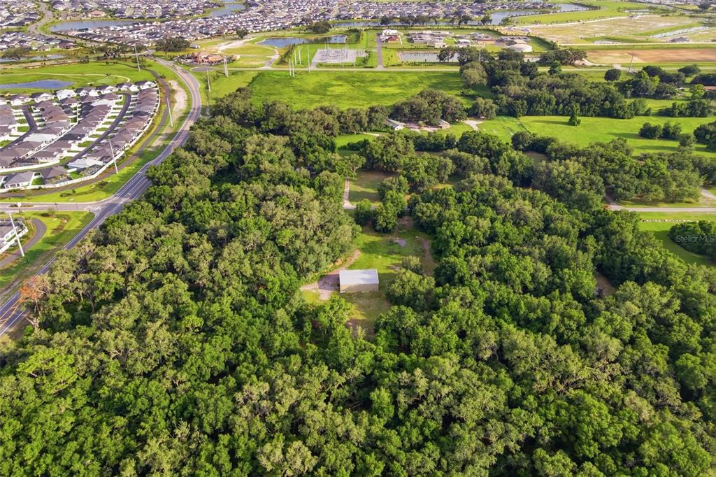 An aerial view shows a small rectangular building surrounded by dense trees and nearby roads — 7112 MARSH BEND TRAIL, WILDWOOD, FL