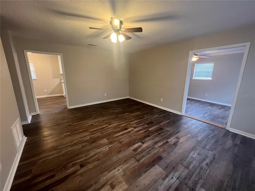 An empty living room features dark wood-look flooring, gray walls, and a ceiling fan — 610 PATLIN AVENUE, ORANGE CITY, FL