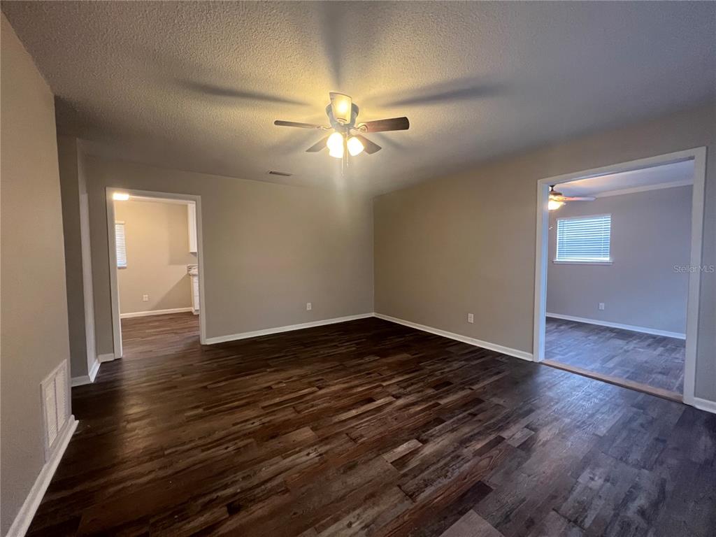 An empty room with dark wood-look flooring, beige walls, and a ceiling fan — 610 PATLIN AVENUE, ORANGE CITY, FL