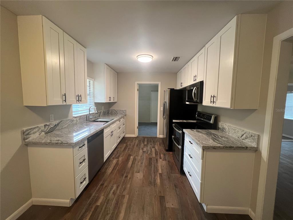 A galley kitchen features white cabinets, granite countertops, stainless steel appliances, and wood-look flooring — 610 PATLIN AVENUE, ORANGE CITY, FL