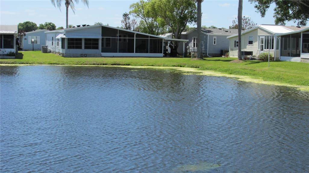 A pond sits in front of several manufactured homes with screened-in porches on a sunny day — 91 STRAPHMORE DRIVE, HAINES CITY, FL