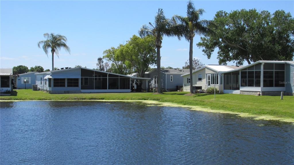 A row of mobile homes sits along the edge of a pond under a blue sky — 91 STRAPHMORE DRIVE, HAINES CITY, FL