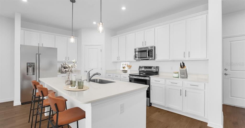 A modern kitchen features white cabinetry, stainless steel appliances, a center island, and wood flooring — 3836 SENNA WAY, TAVARES, FL