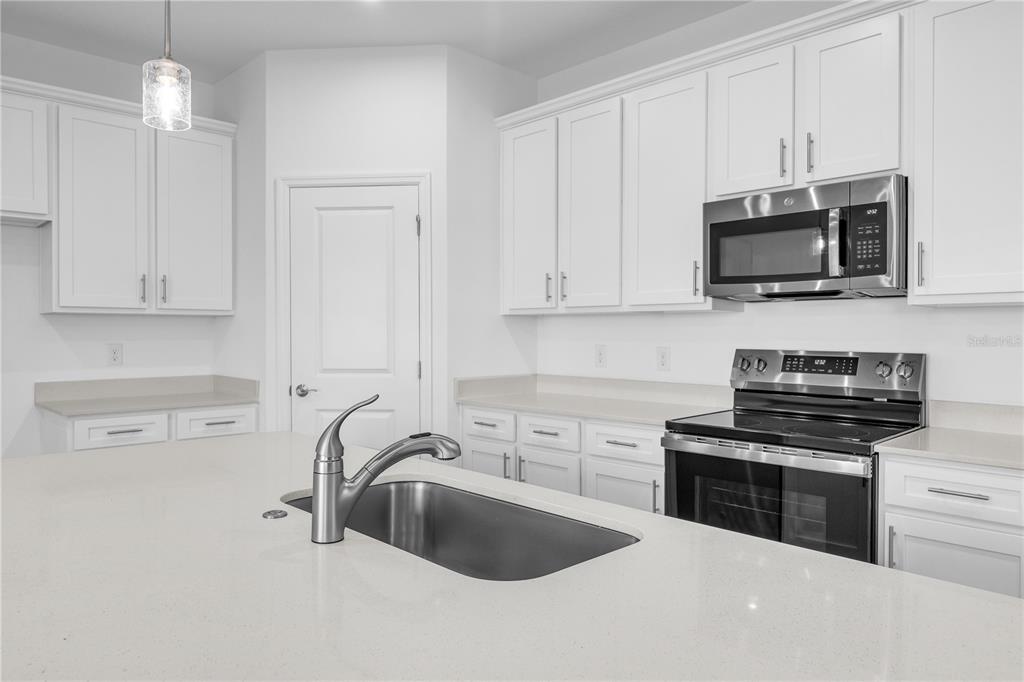 A modern kitchen features white cabinetry, quartz countertops, a stainless steel oven, and a sink island — 3836 SENNA WAY, TAVARES, FL