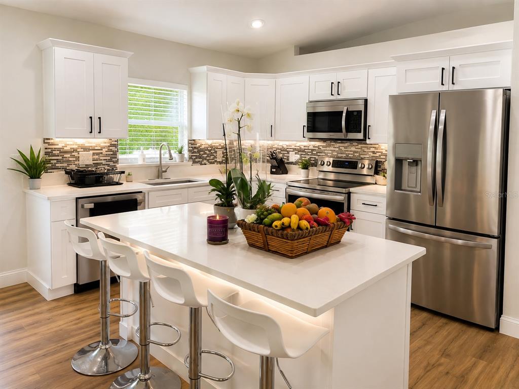 A modern kitchen features white cabinetry, stainless steel appliances, and a central island with seating — 25546 BRUFORD BOULEVARD, LAND O LAKES, FL