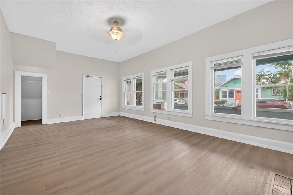 An empty room with light wood-look flooring, white walls, and several windows overlooking a street — 633 7TH AVENUE N, ST PETERSBURG, FL