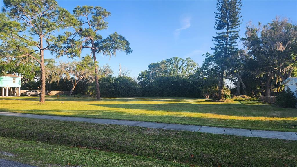 A wide, grassy vacant lot features several mature trees under a clear blue sky — 4TH AVE SW, RUSKIN, FL