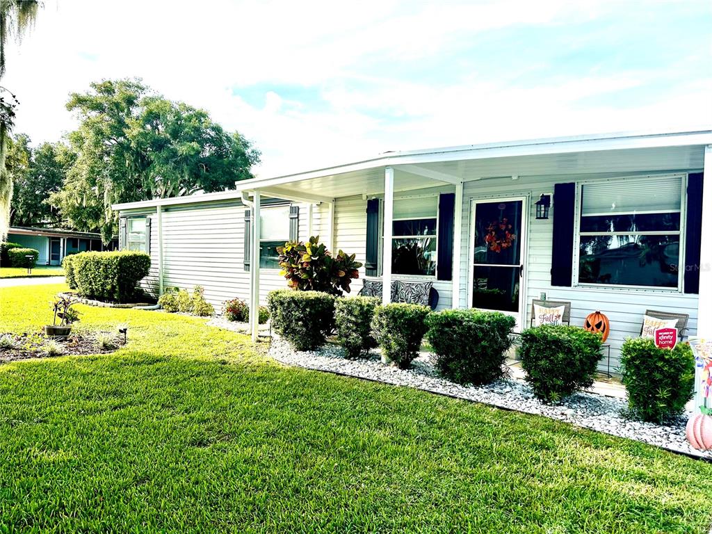 A single-story mobile home features light siding, a covered front porch, and manicured landscaping — 2409 VINDALE ROAD, TAVARES, FL