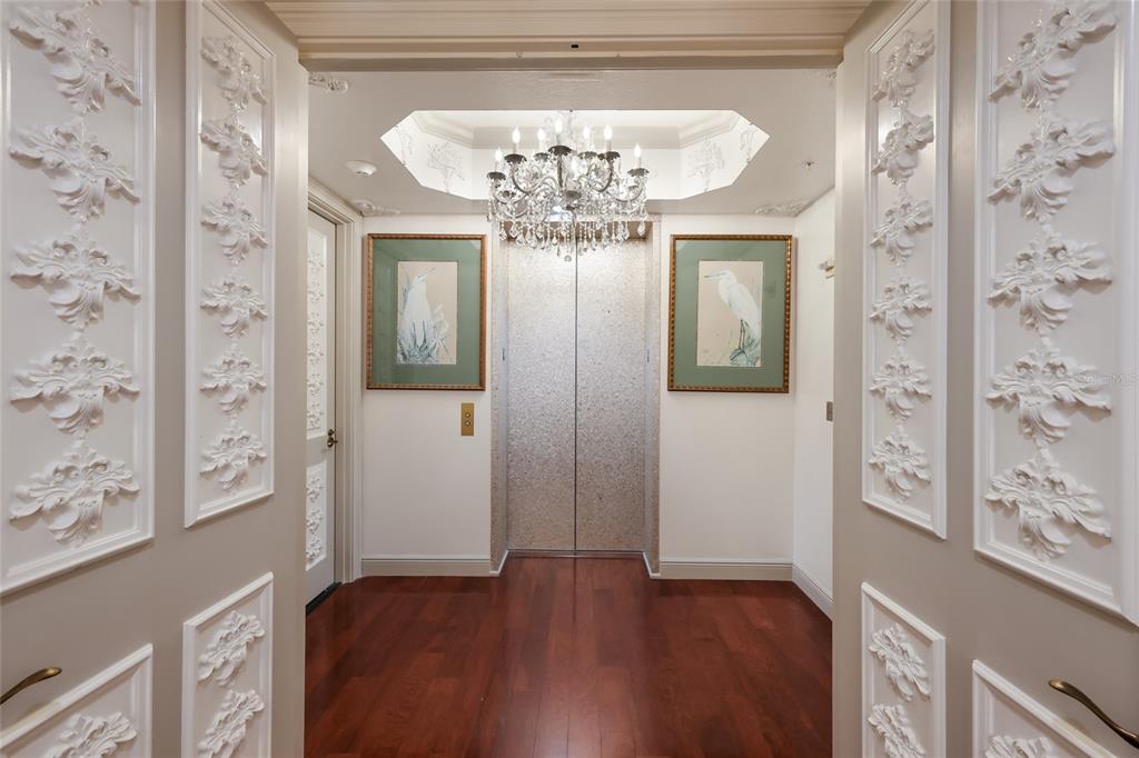 A formal foyer features a private elevator, hardwood floors, ornate wall molding, and a chandelier — 35 WATERGATE DRIVE UNIT 804, SARASOTA, FL