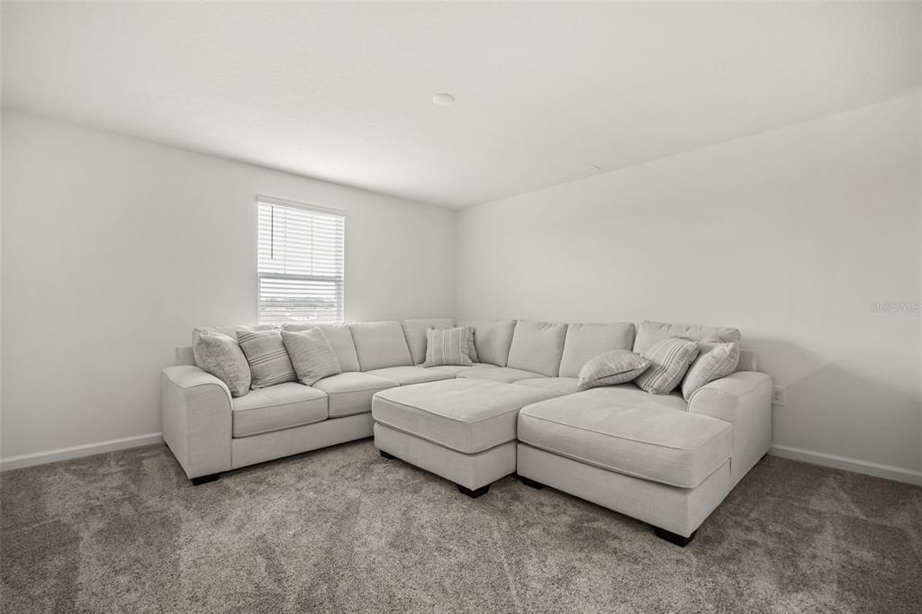A living room features a large light-gray sectional sofa on carpeted flooring near a window — 4981 WORCHESTER DRIVE, KISSIMMEE, FL