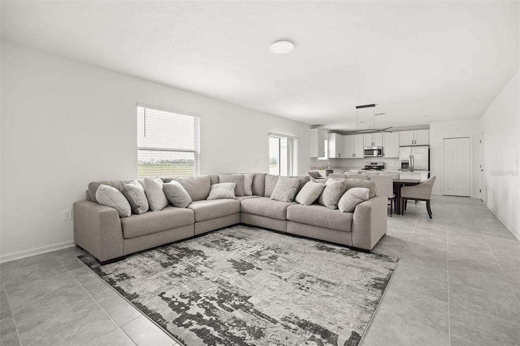 A spacious living room with a large sectional sofa, area rug, and open kitchen beyond — 4981 WORCHESTER DRIVE, KISSIMMEE, FL