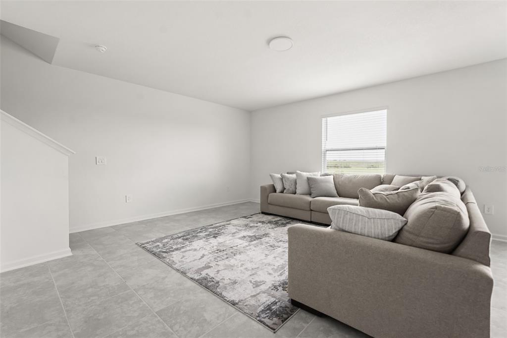 A living room with light gray tile flooring, a large sectional sofa, and a rug — 4981 WORCHESTER DRIVE, KISSIMMEE, FL
