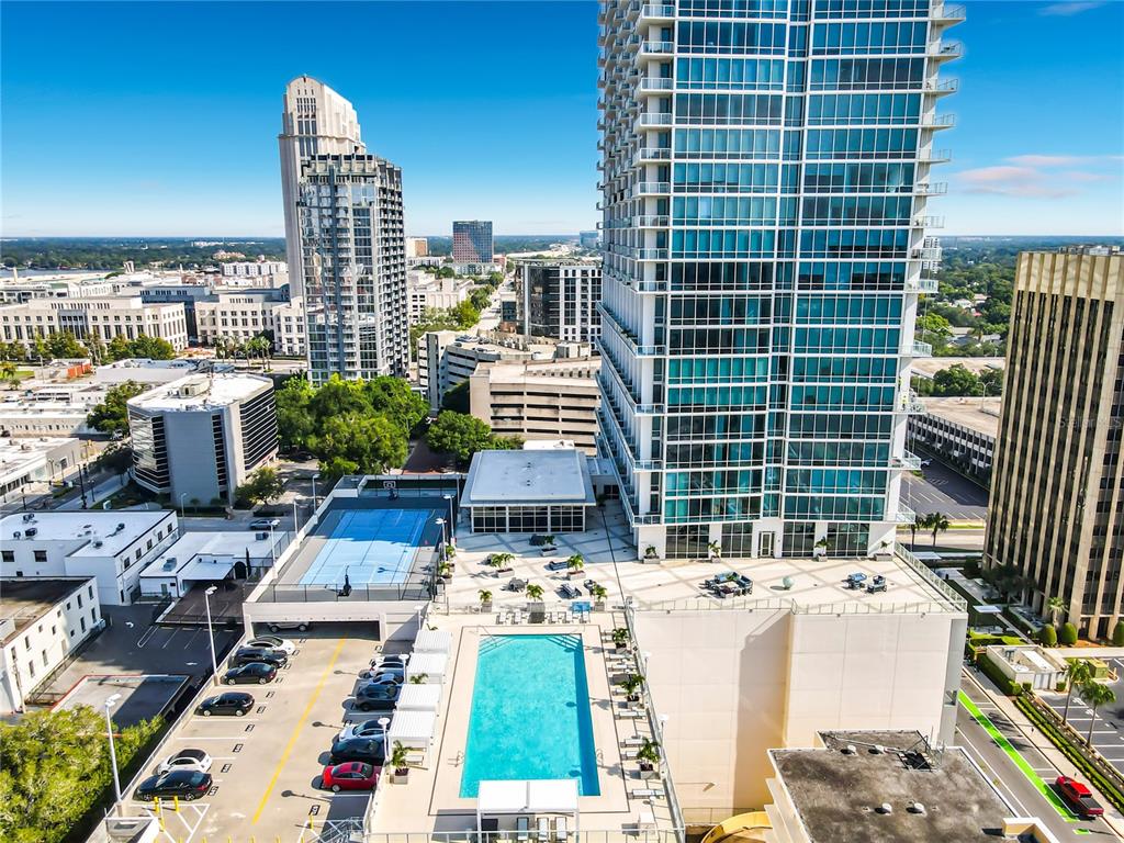 An aerial view shows a high-rise building with a rooftop pool, tennis court, and parking — 150 E ROBINSON STREET UNIT 617, ORLANDO, FL