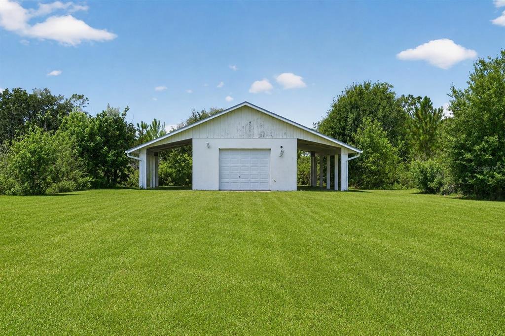A white detached garage with open-sided covered wings sits in a large grassy yard — 5300 CYPRESS GROVE, PUNTA GORDA, FL