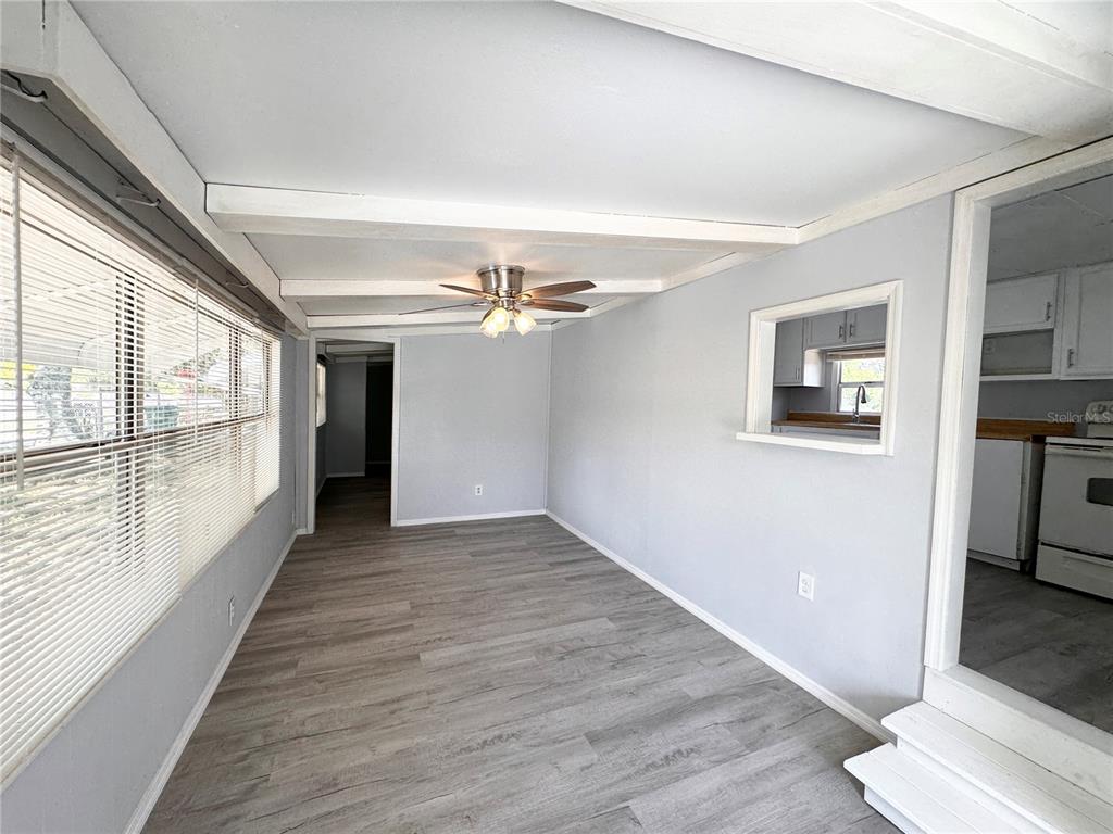 A room with light gray walls, wood-look flooring, a ceiling fan, and a kitchen pass-through — 3418 BROCKETT ROAD, MIMS, FL