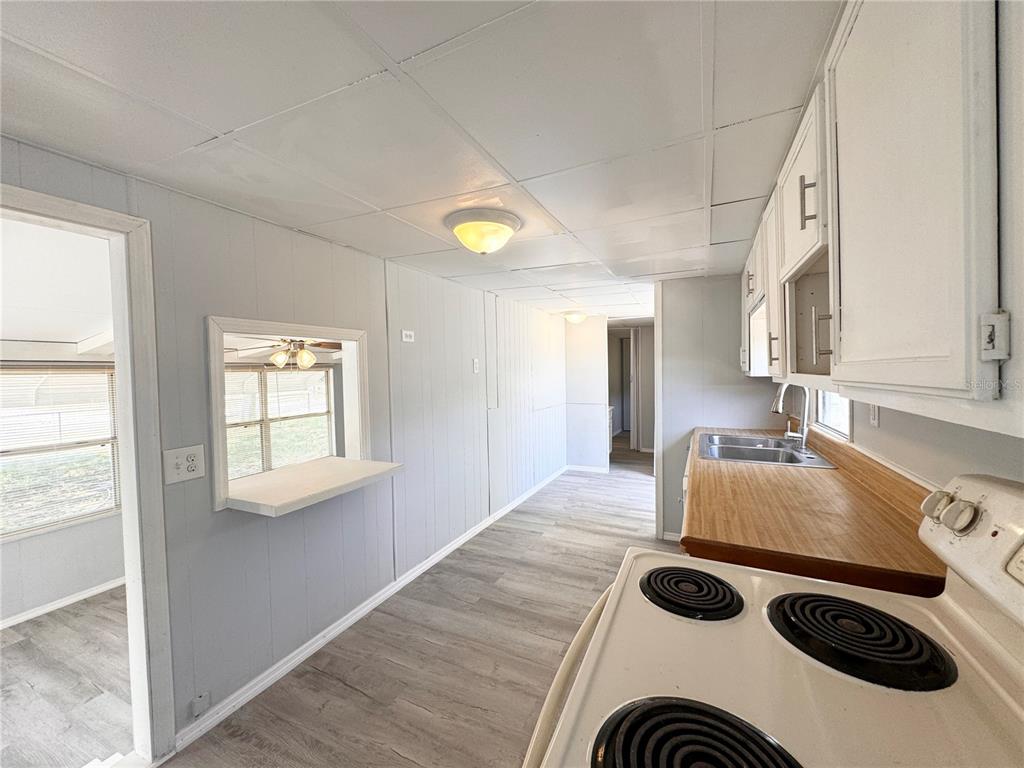 A kitchen with white cabinets, a wood-look countertop, and a pass-through window to another room — 3418 BROCKETT ROAD, MIMS, FL