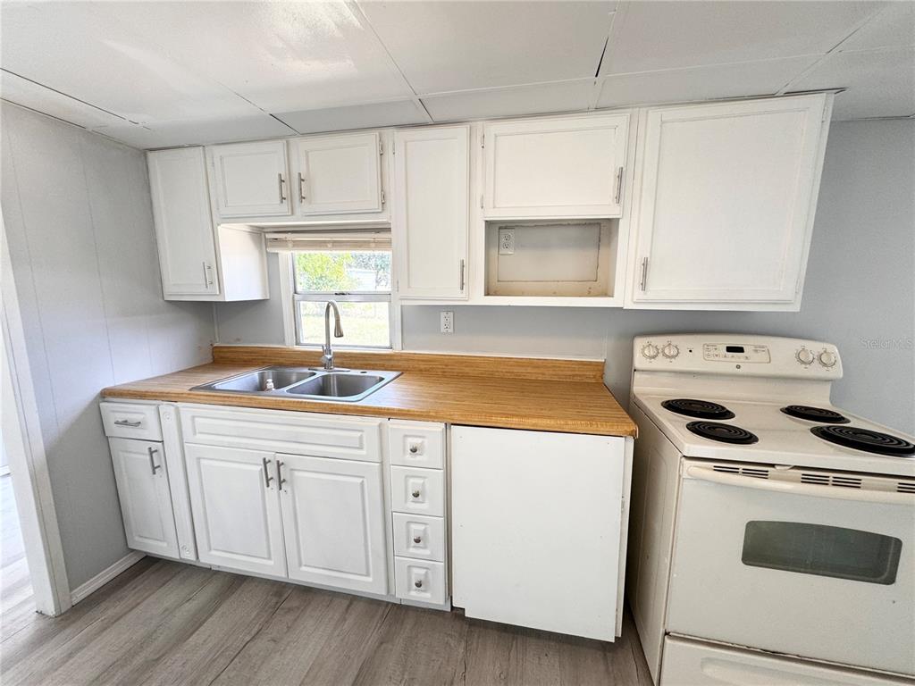 A kitchen features white cabinets, a wood-look laminate countertop, a double sink, and a stove — 3418 BROCKETT ROAD, MIMS, FL