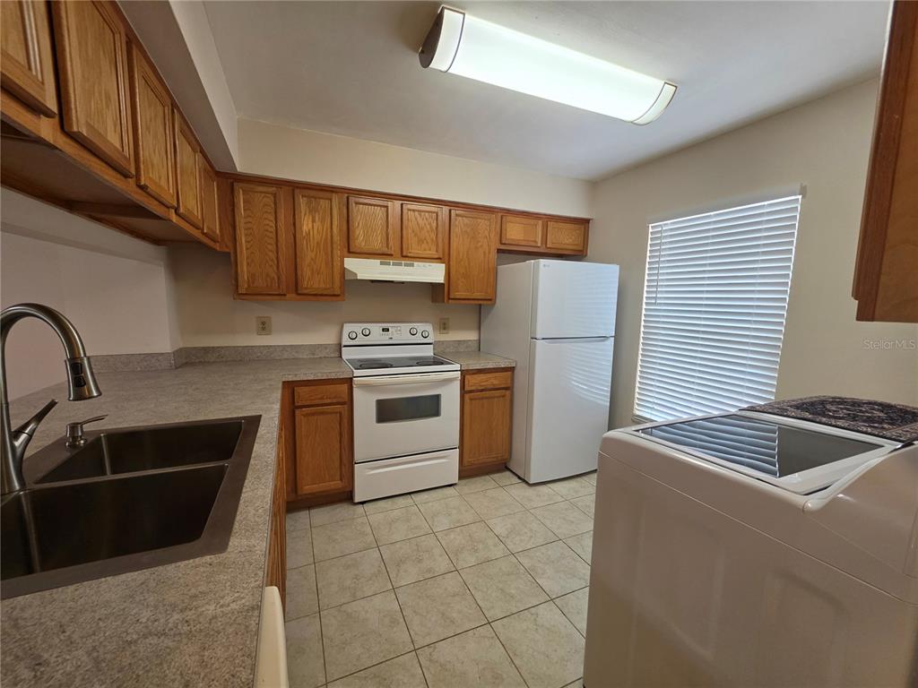 A kitchen features wood cabinets, white appliances, a double sink, and tile flooring — 5202 SUNRIDGE PALMS DRIVE UNIT 5202, TAMPA, FL