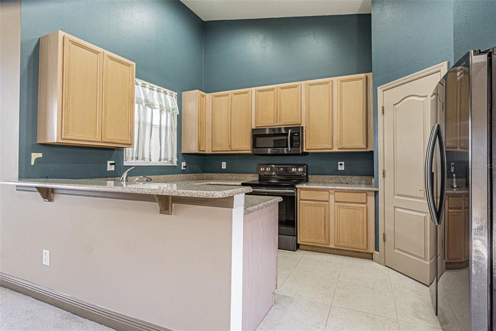 A kitchen features light wood cabinets, granite countertops, dark teal walls, and stainless steel appliances — 9506 ROLLING CIRCLE, SAN ANTONIO, FL
