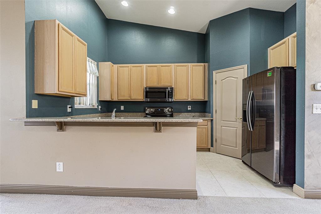 A kitchen features light wood cabinets, dark teal walls, granite countertops, and black appliances — 9506 ROLLING CIRCLE, SAN ANTONIO, FL