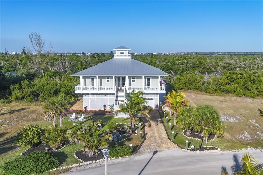 An elevated house with a metal roof and wraparound porch sits in a grassy landscape — 7121 RUM BAY DRIVE, PLACIDA, FL